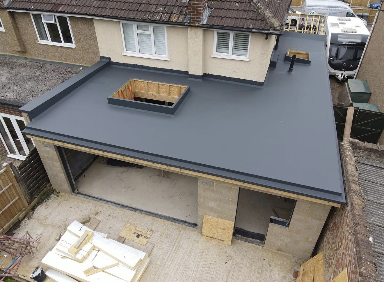 New grey single-ply flat roof on a brick garage extension with a rooflight opening, viewed from above