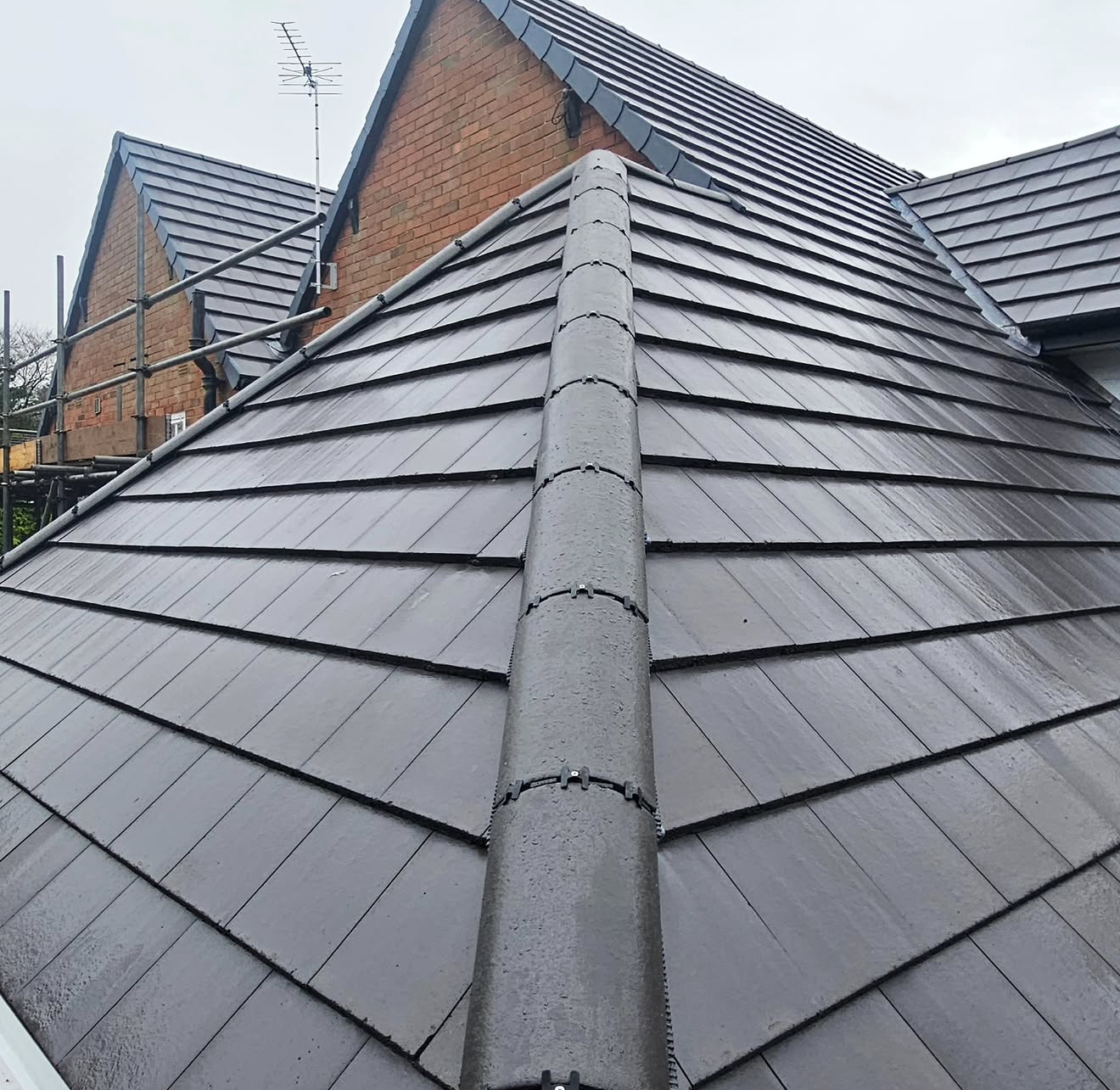 Grey concrete tiled roof with mechanically fixed concrete ridge tiles and scaffolding