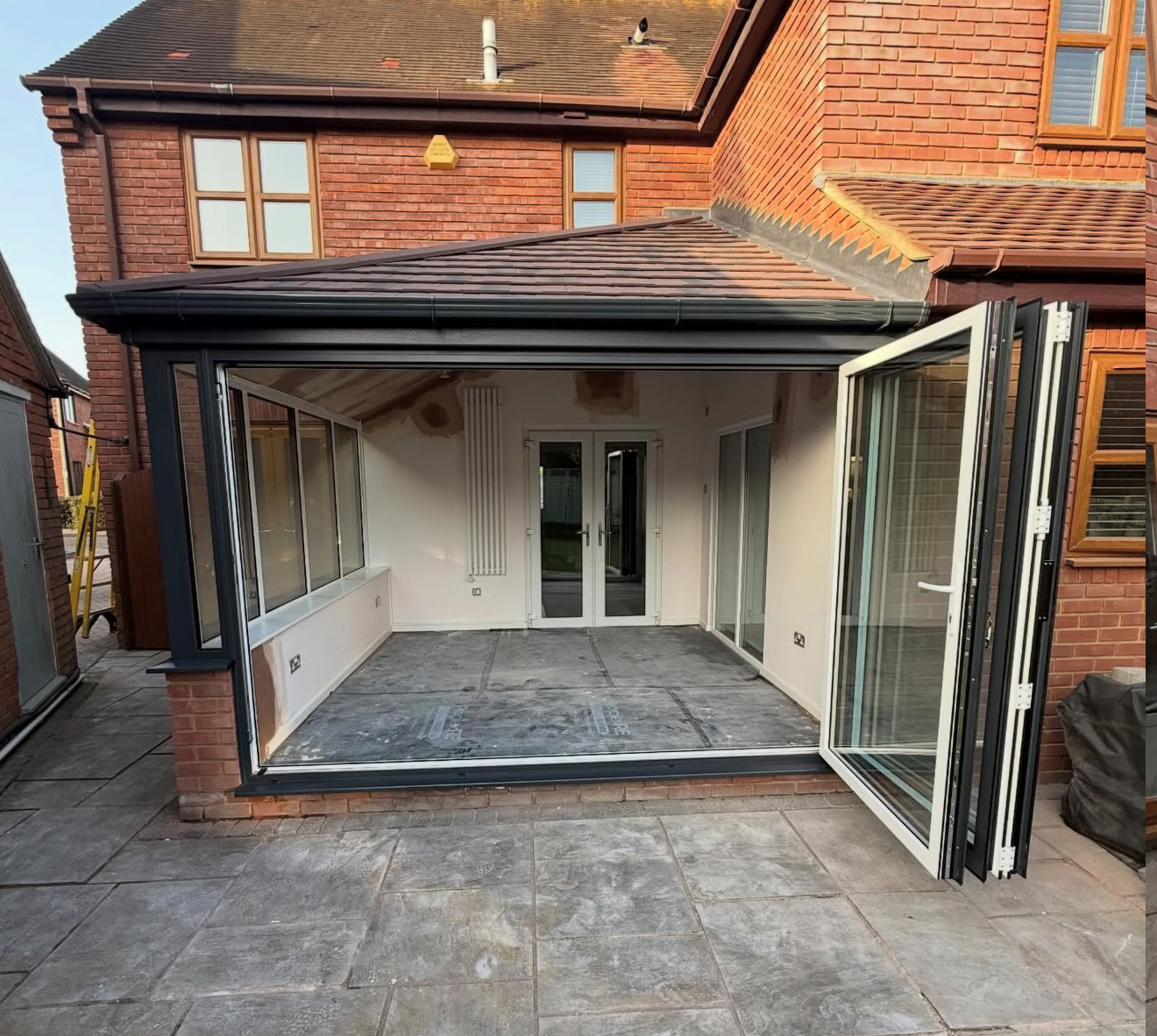Open-plan conservatory extension with a brown tiled roof, dark frames and folding glazed doors