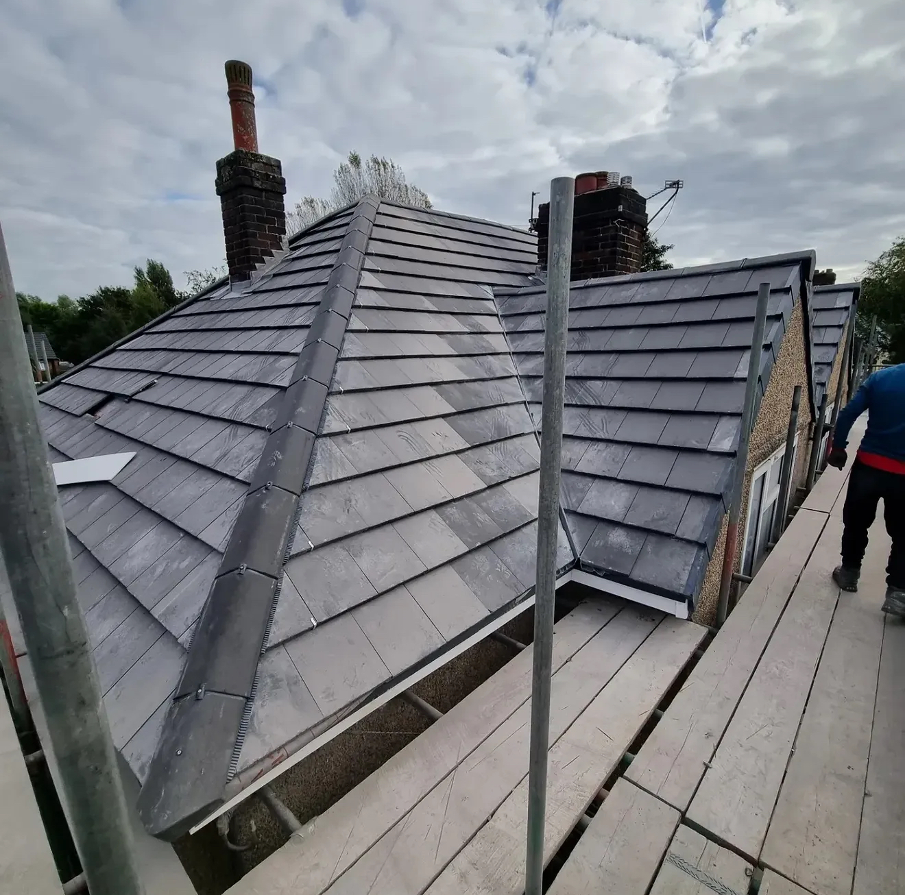 Grey tiled roof with central ridge and lead valley, viewed from a scaffolding walkway