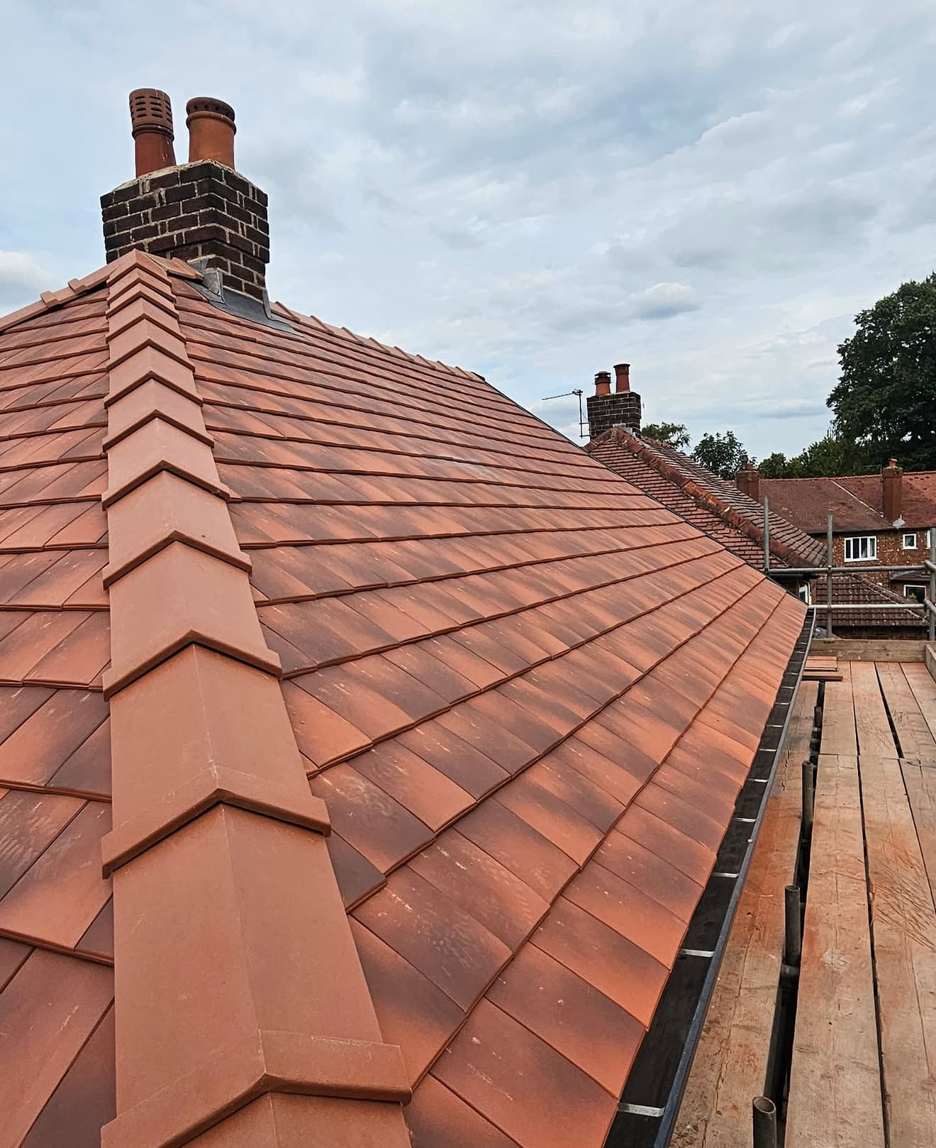 Terracotta clay tiled roof with bonnet hip tiles and traditional chimney pots