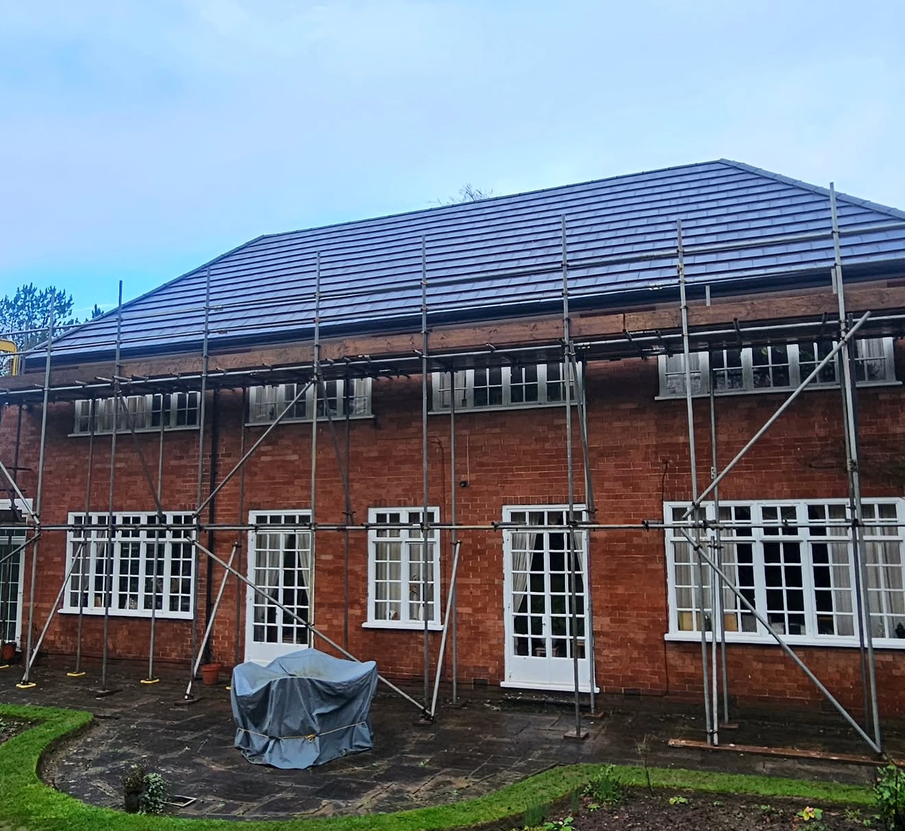 Red brick house under full scaffolding with a new dark tiled roof in progress