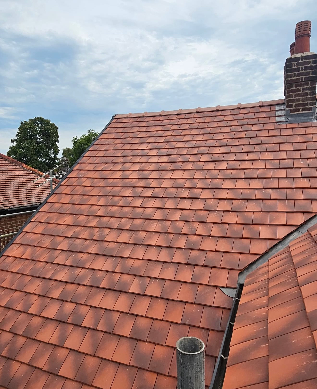 Sweeping terracotta clay tiled roof with chimney and neighbouring rooftops
