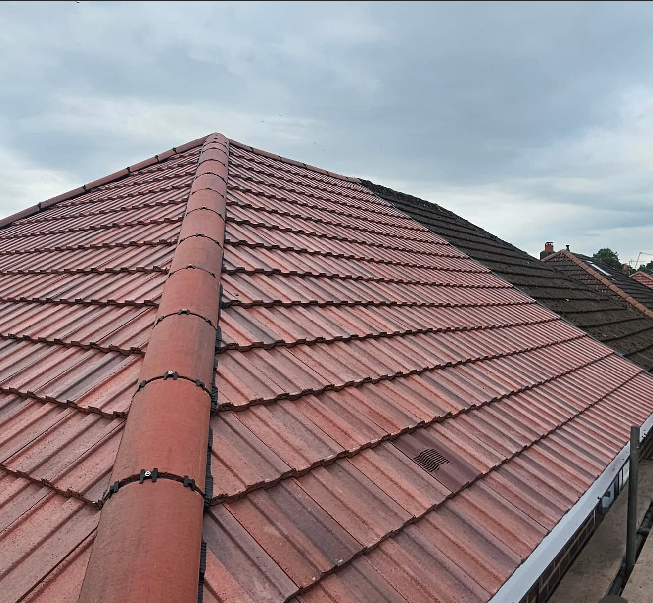 Close view of red interlocking roof tiles and half-round ridge tiles against the sky
