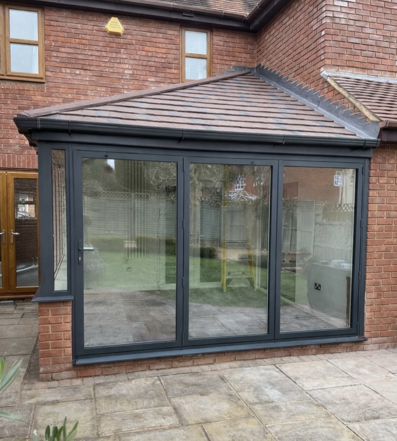 Completed conservatory with a brown tiled hipped roof, dark frames and glazed frontage