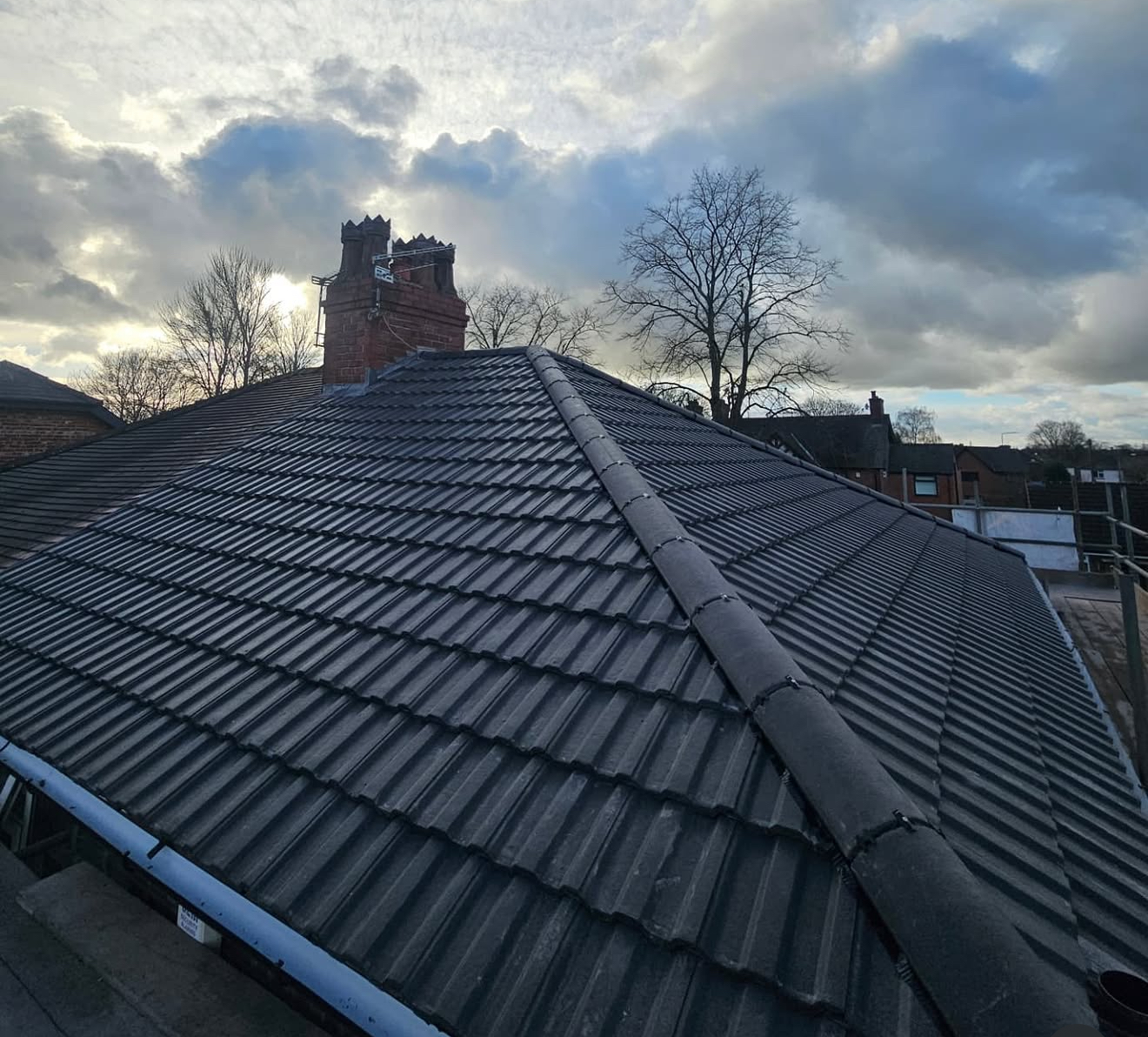 Dark interlocking tiled roof and brick chimney stack photographed at dusk