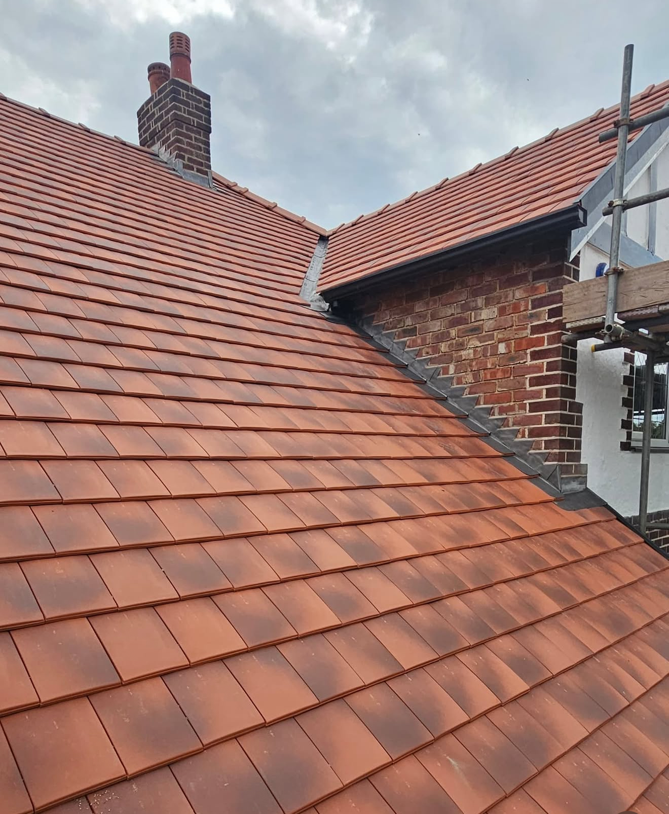 Terracotta clay plain tiled roof with a lead valley and brick chimney stack