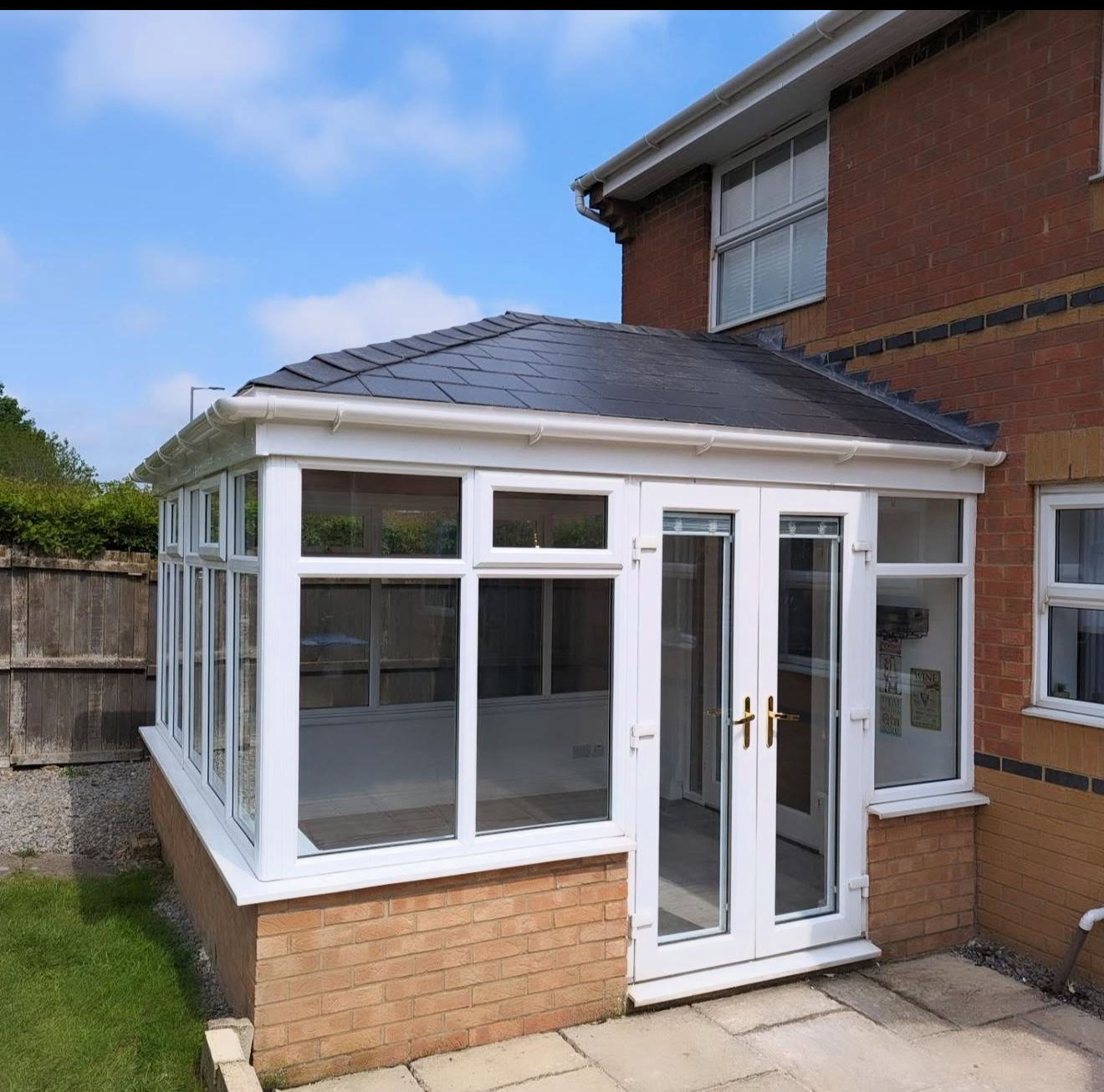 Completed conservatory with a dark slate hipped roof, white frames, glazed doors and brick base