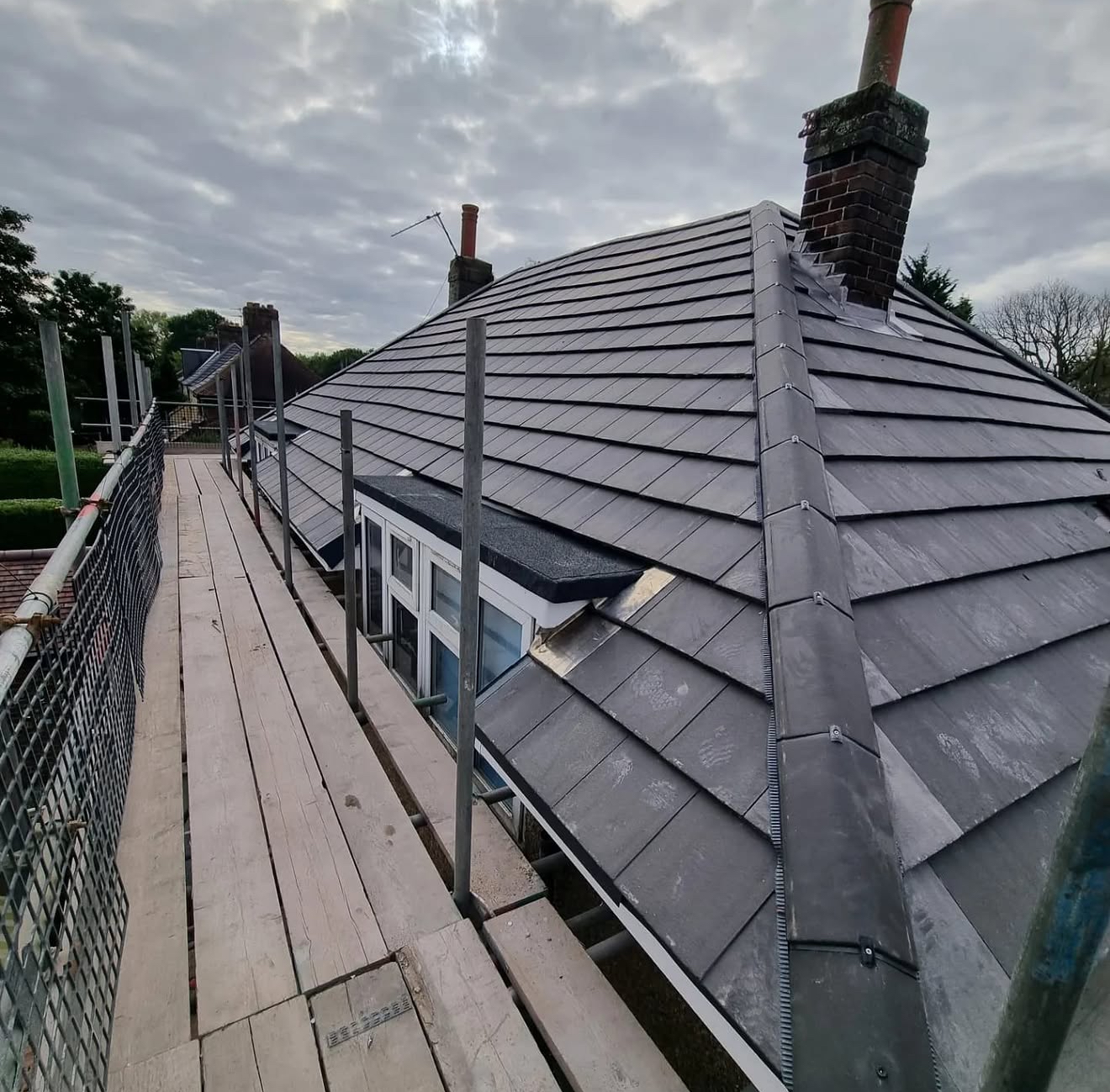 Grey tiled roof with central ridge, dormer window and scaffolding walkway alongside