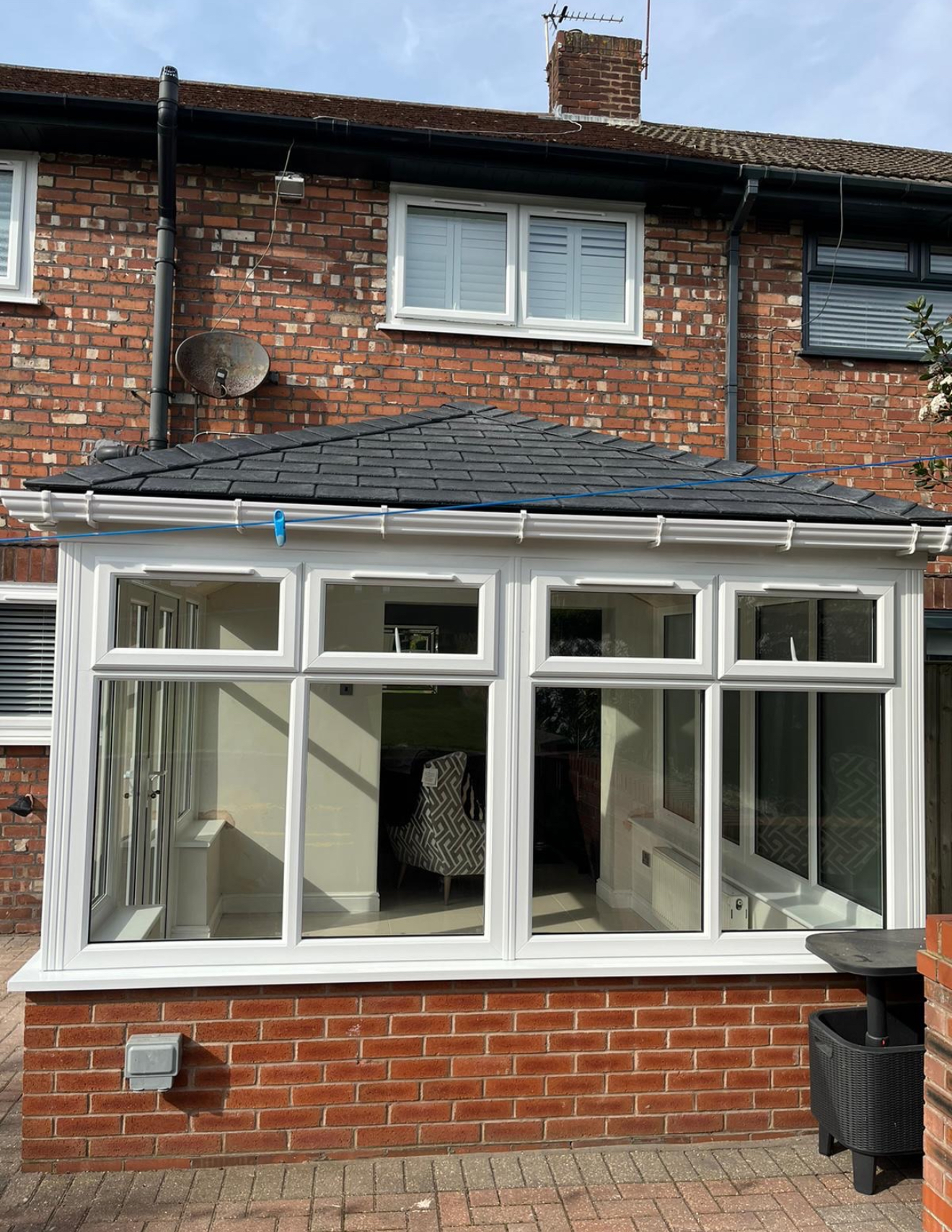 White conservatory with a dark slate hipped roof, guttering and glazed windows
