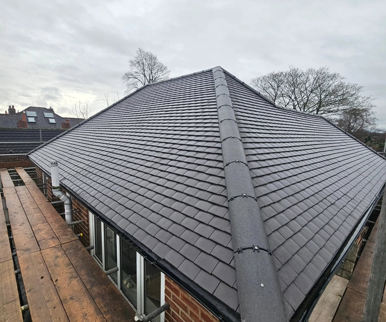 Finished grey slate roof on a detached house with new guttering and ridge line