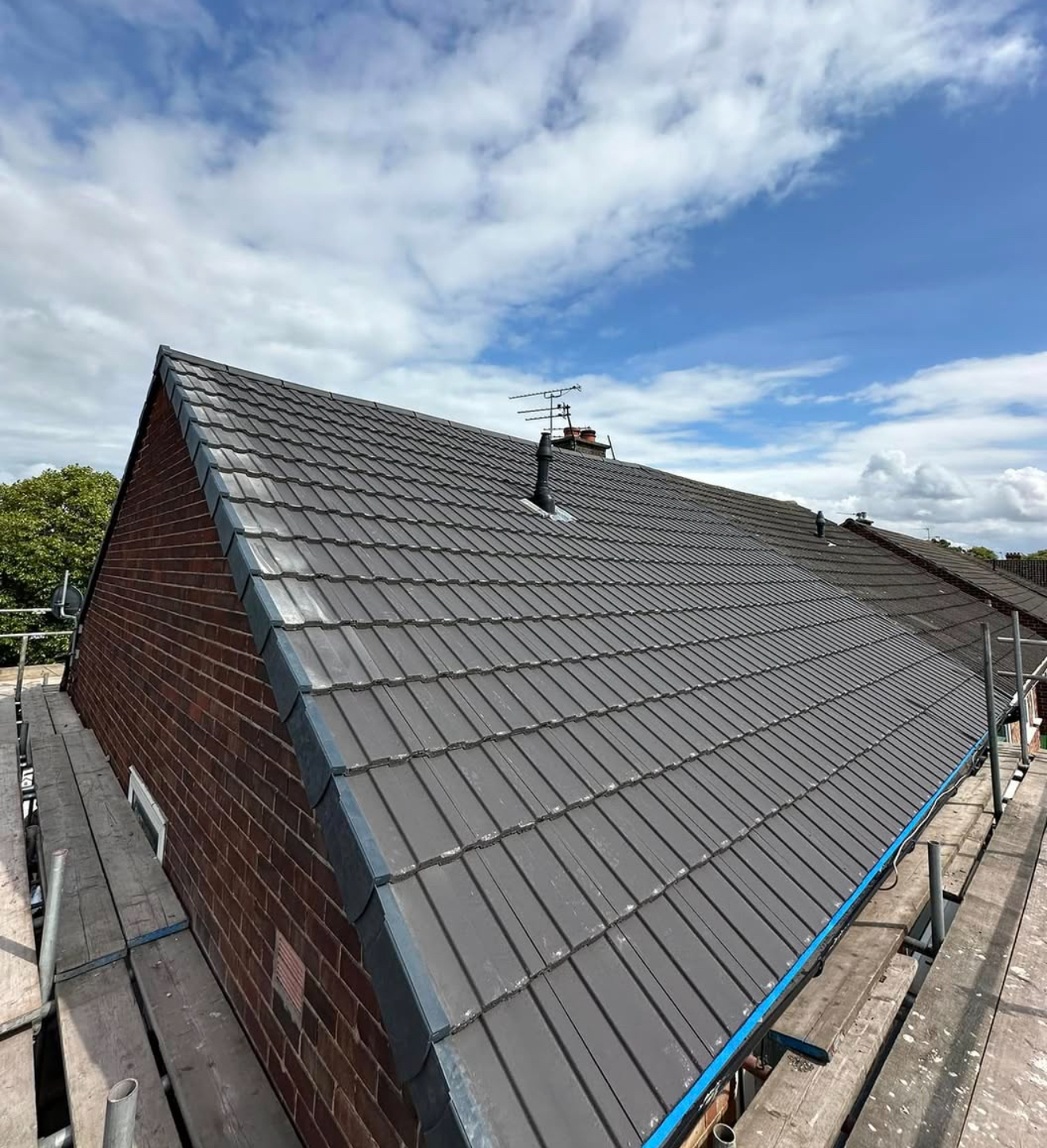 Dark grey interlocking tiled roof with lead valley and verge detailing, photographed in bright weather