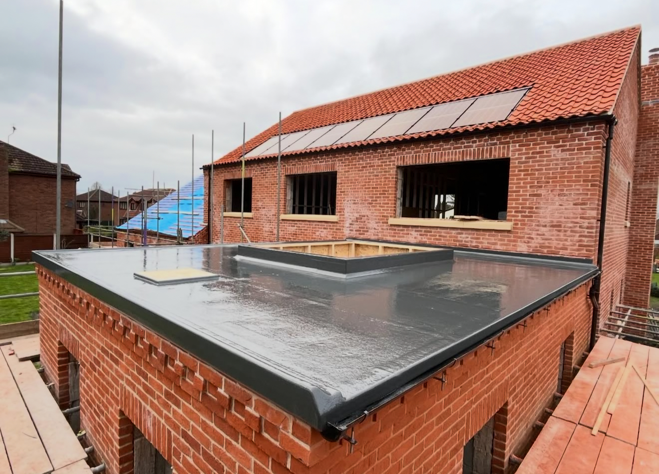 Red interlocking tiled roof with integrated solar panels and a new flat roof section in the foreground