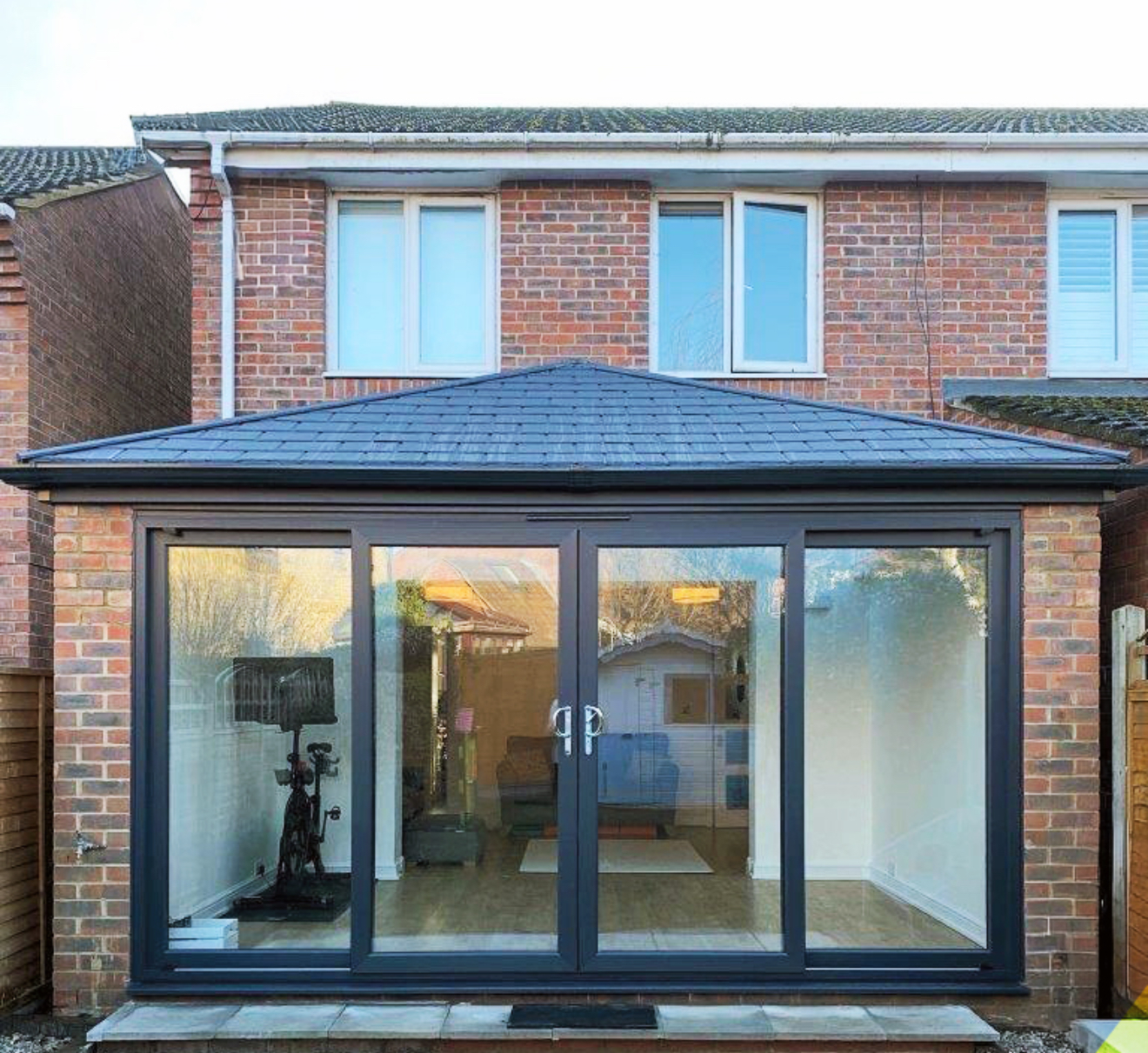 Completed extension with a low-pitched blue-grey tiled roof and dark framed glazed doors